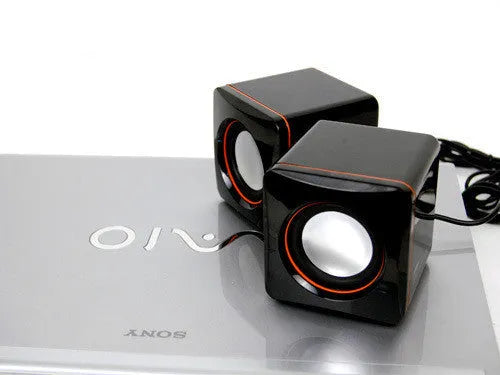 Black small square USB-powered computer speaker on desktop next to monitor