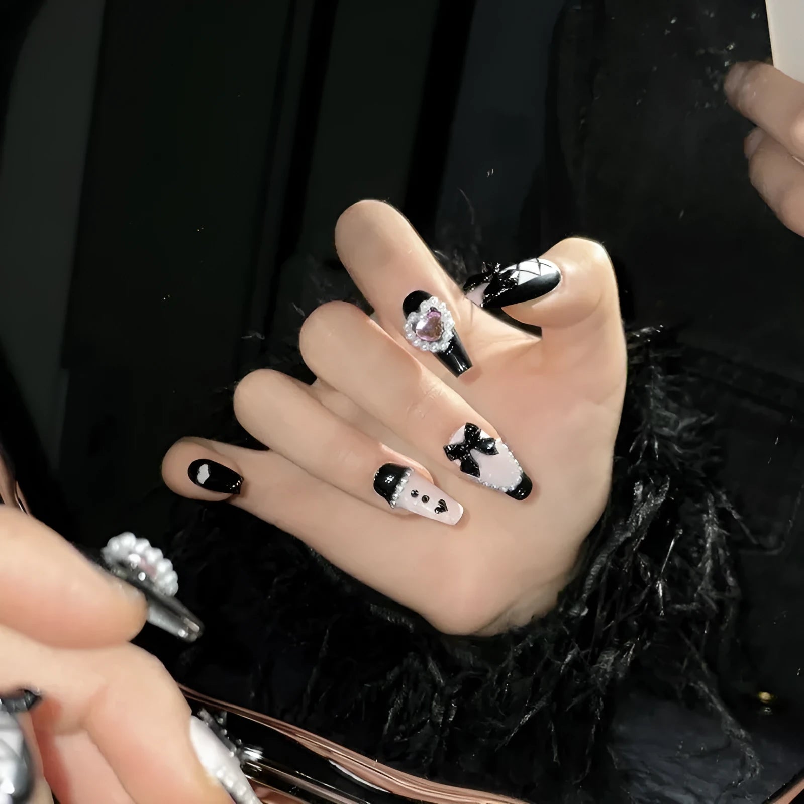 Black and pink heart-shaped hand-painted false nails with bow design, shown in mid-length cat's eye style.