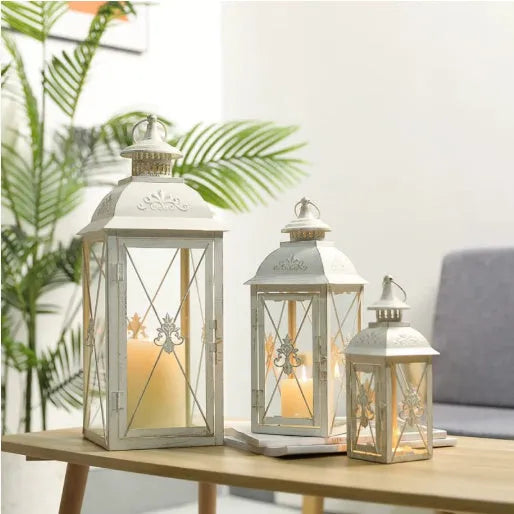 Black and gold wrought iron floor-standing storm lantern with tempered glass panes on a stone patio.