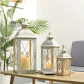 Black and gold wrought iron floor-standing storm lantern with tempered glass panes on a stone patio.