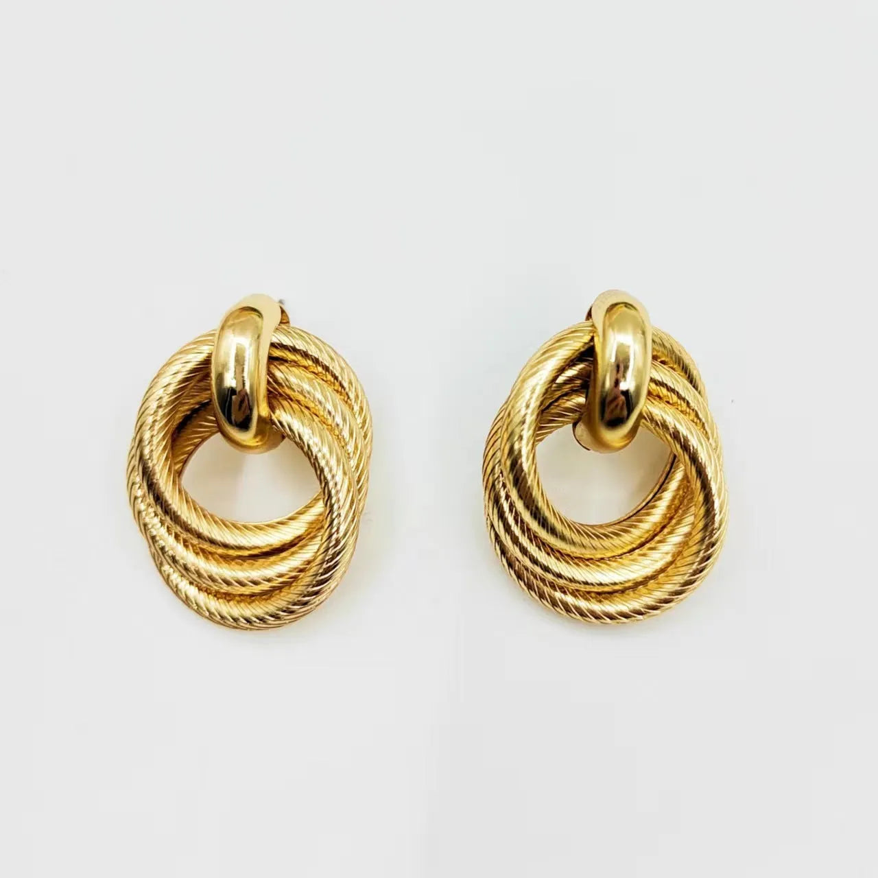 Geometric ring embossed twisted metal stud earrings in gold colour on a plain background