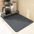Black square rubber-backed kitchen drying mat on a countertop next to a coffee cup