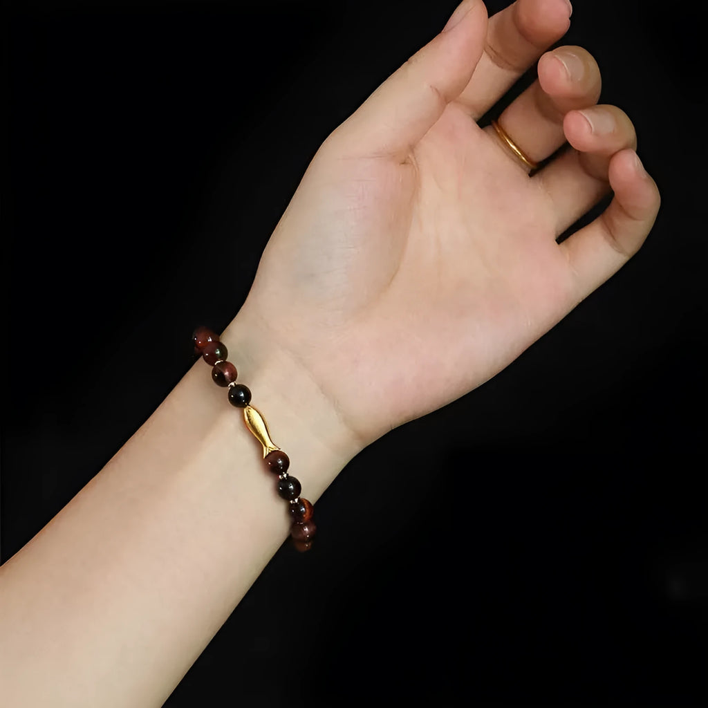 Close-up of a yellow tiger eye beaded bracelet with a detailed small fish charm.