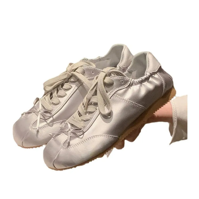Women's silver satin ballet flats with round toe and white front lace-up on a rubber sole.