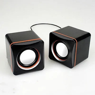 Black small square USB-powered computer speaker on desktop next to monitor