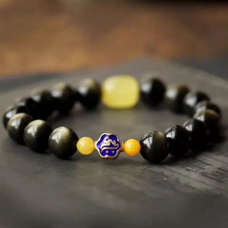 Handmade golden obsidian bracelet with geometric beads and zodiac charm on wrist.