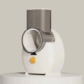 White electric vegetable slicer with rotary grater, feeding port, and multiple blade options on kitchen counter