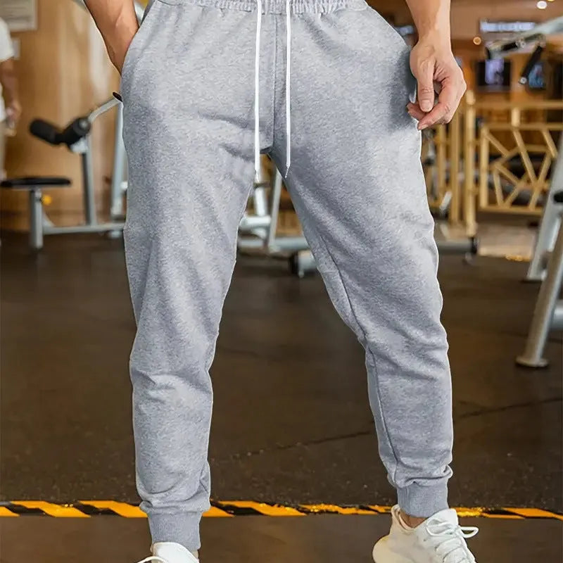 Man wearing beige linen-style loose fit trousers with an elastic drawstring waist.