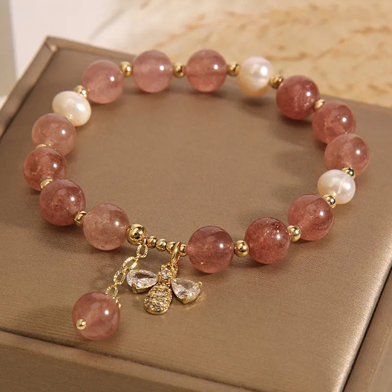 Close-up of a women's bracelet with strawberry quartz, freshwater pearls, a bee charm, and zircon accents on an alloy chain.