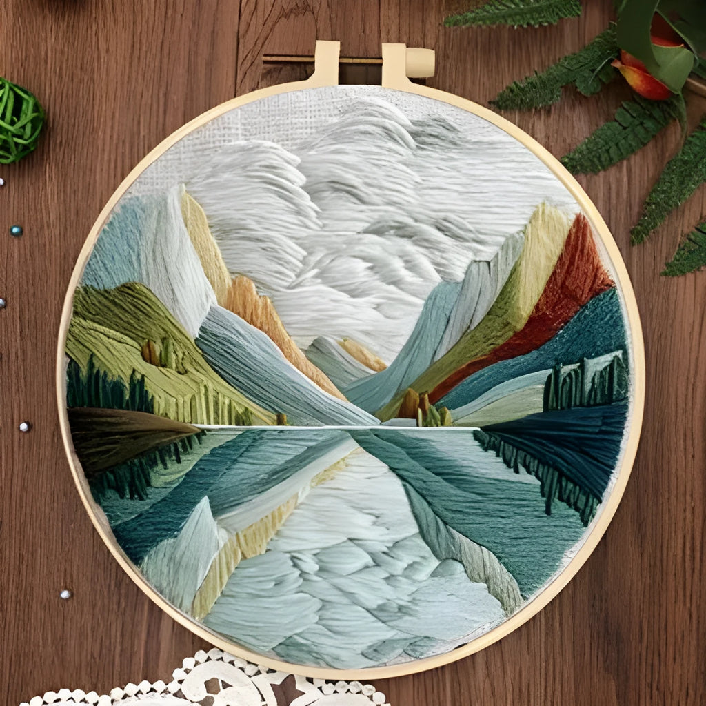 DIY embroidery kit components: printed cotton landscape fabric, embroidery threads, needles, and a bamboo hoop.