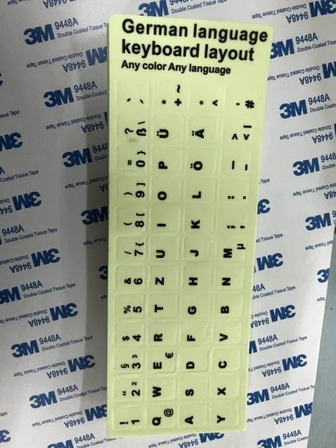 Yellow PVC sheet of glow-in-the-dark keyboard stickers for Arabic, Thai, Hebrew, French, Italian, and German layouts.