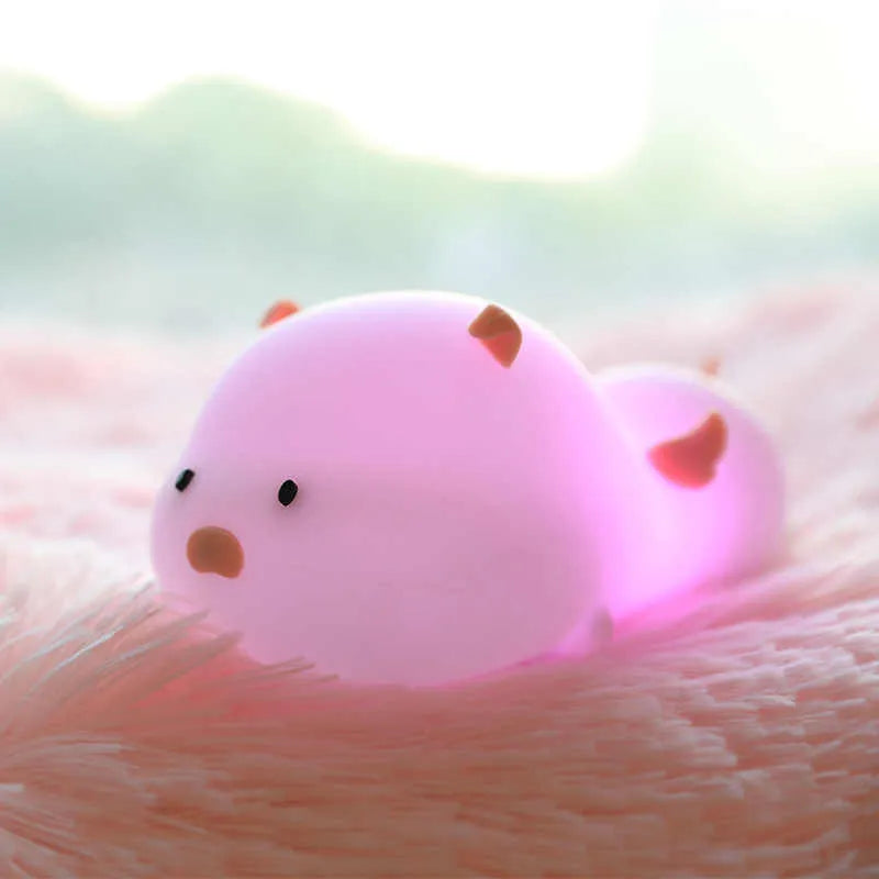 Blue rechargeable pig-shaped silicone night light with a sleeping design on a bedside table.