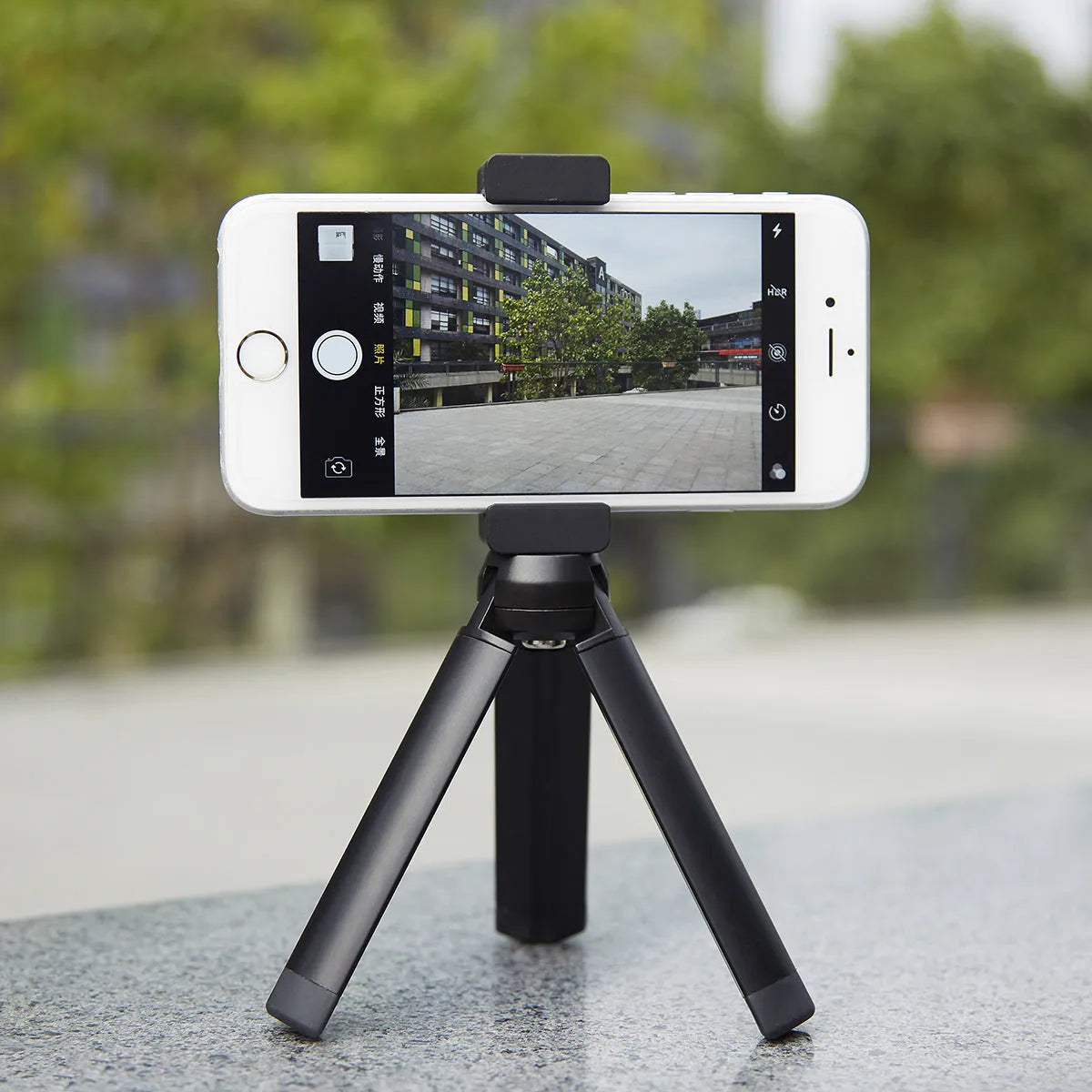 Silver aluminium smartphone bracket for tripod mounting next to a mobile phone.