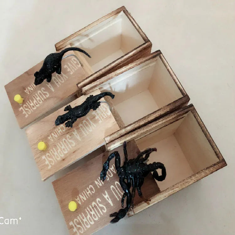 Wooden prank box with lid open showing a lifelike jumping spider inside on a white background.