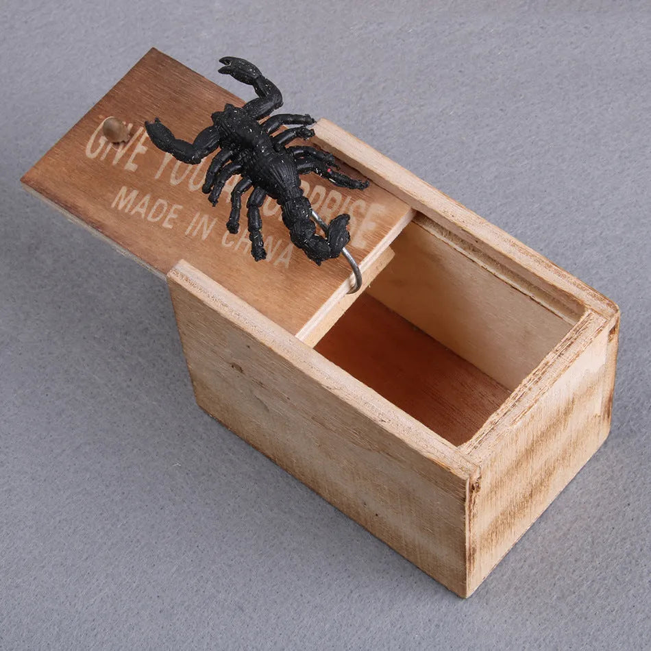 Wooden prank box with lid open showing a lifelike jumping spider inside on a white background.