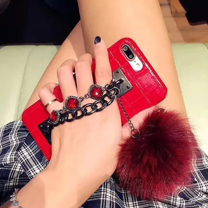 Red PU leather iPhone case with rhinestone studs and a white fox fur ball charm attached.