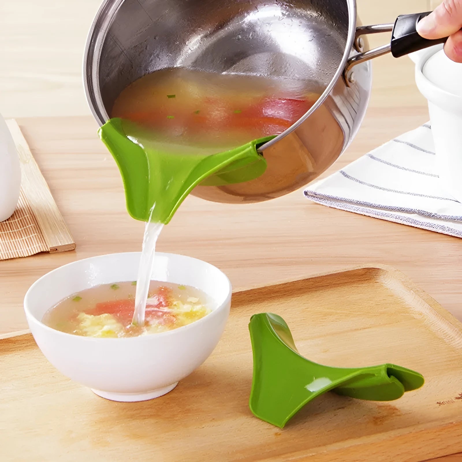 Green silicone clip-on kitchen funnel for pouring liquids into round pots.