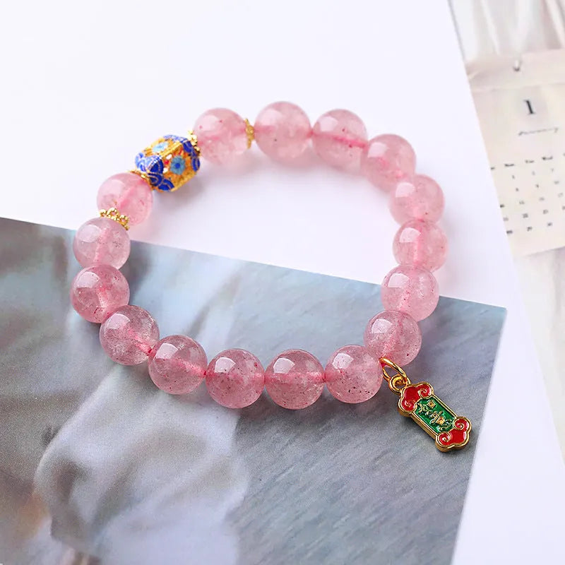 Close-up of a pink Strawberry Quartz crystal bracelet with hand-woven beads and a golden Ruyi symbol charm.