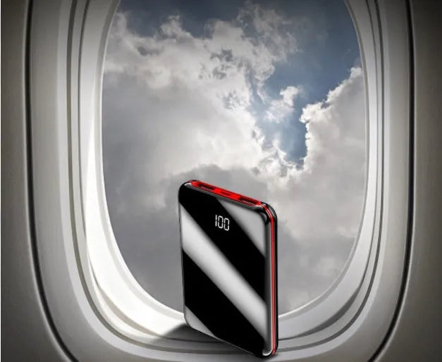 Black mini power bank with digital LCD screen showing battery percentage, next to a smartphone.