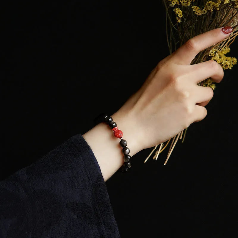 Natural obsidian bracelet with round beads and red cinnabar fungus decoration on wrist
