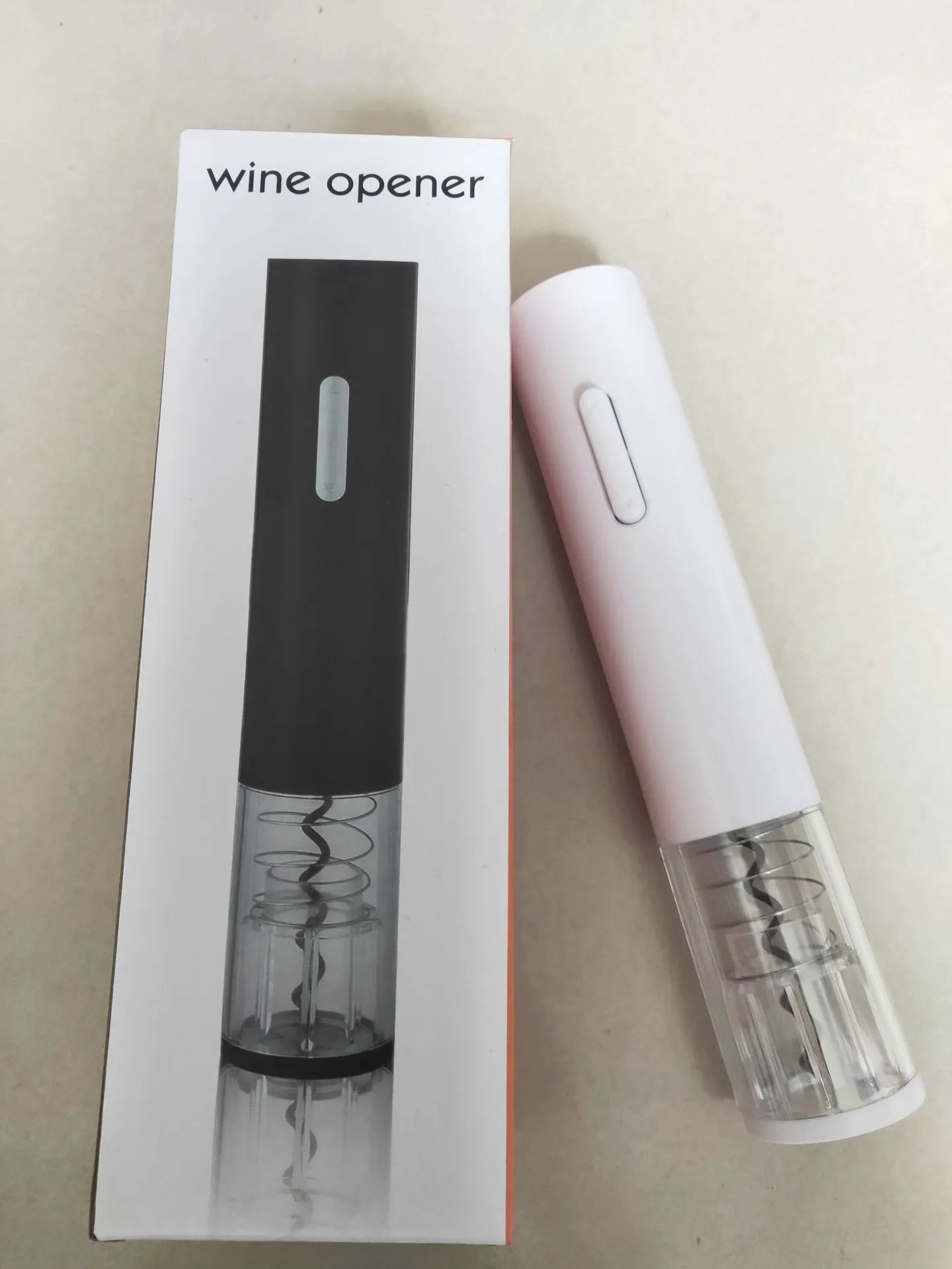Black automatic electric wine bottle opener with foil cutter on a wooden table next to a wine bottle.