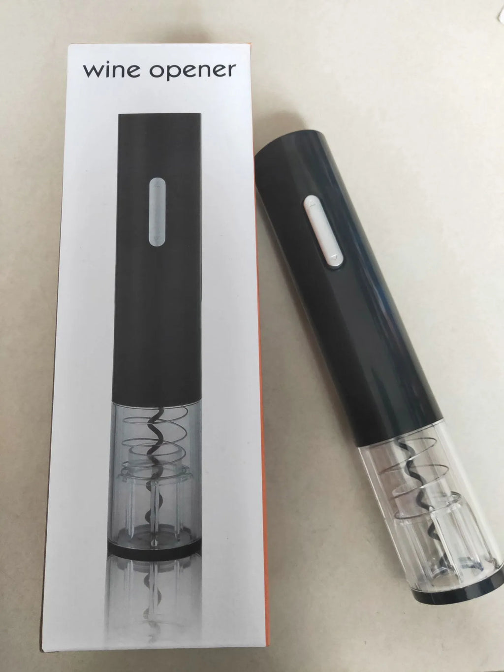 Black automatic electric wine bottle opener with foil cutter on a wooden table next to a wine bottle.