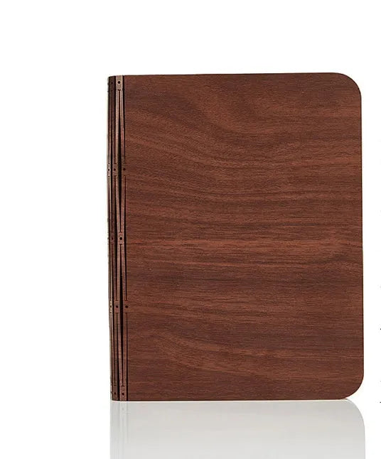 A solid wood adjustable LED book light on a desk next to a book.