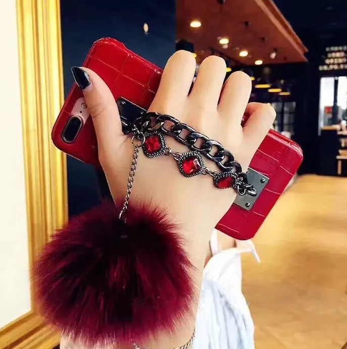Red PU leather iPhone case with rhinestone studs and a white fox fur ball charm attached.