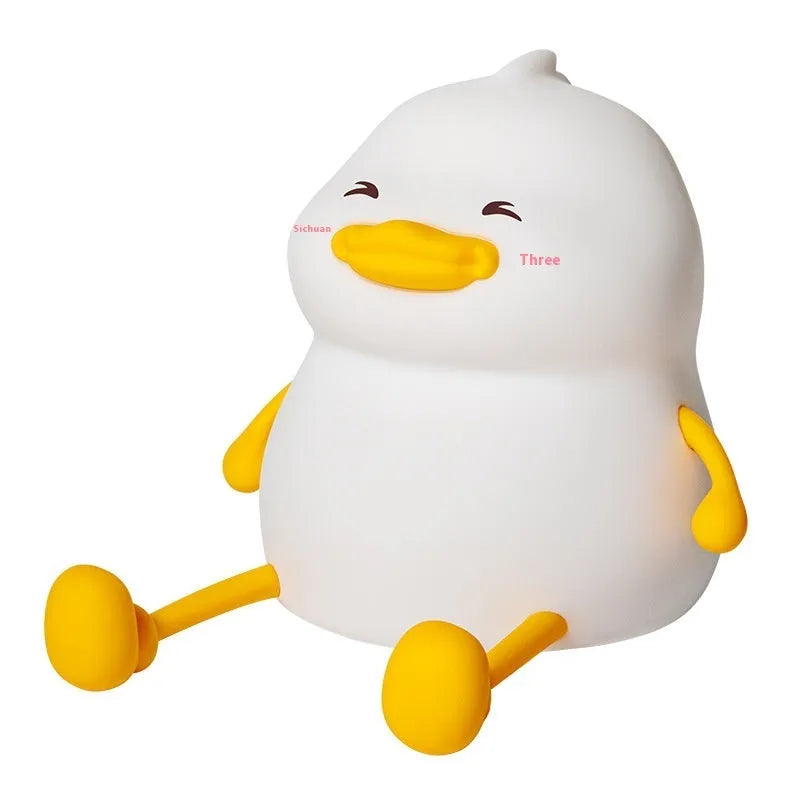 Chubby white silicone night light on a desk holding a mobile phone, showing touch controls and USB port.