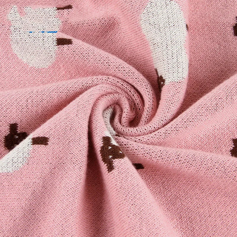 Grey and pink baby sheepskin blanket measuring 100cm by 80cm on a crib