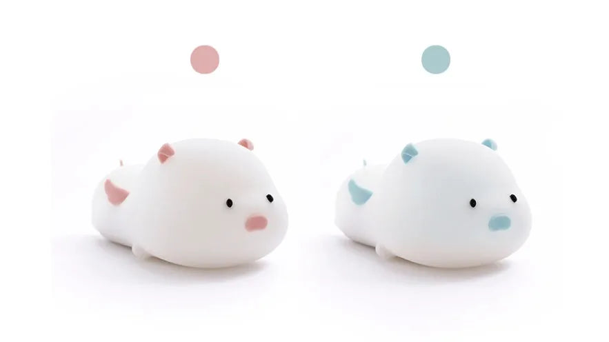 Blue rechargeable pig-shaped silicone night light with a sleeping design on a bedside table.