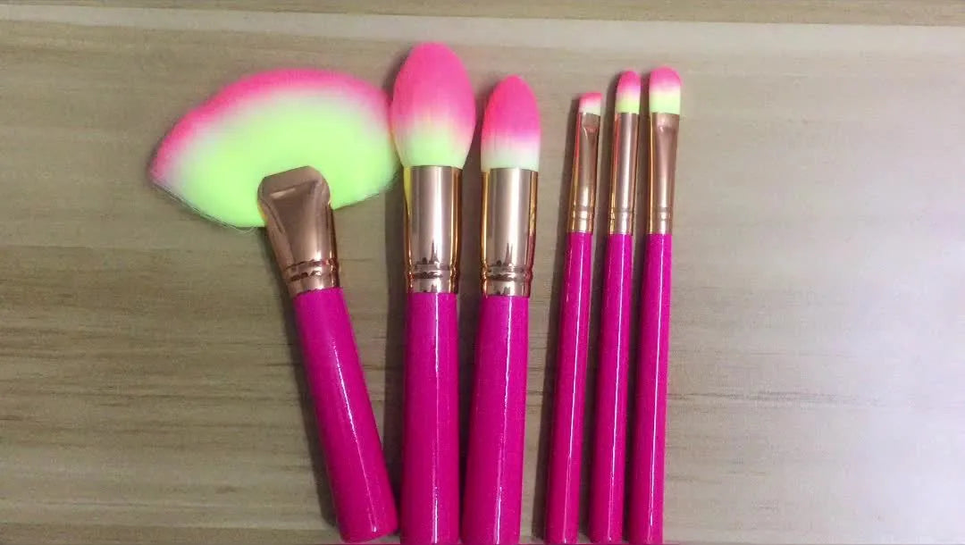 Pink cosmetic makeup brush set with wooden handles and synthetic bristles laid out on a surface