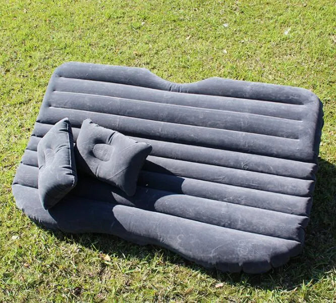 Inflatable car bed with flocking material shown in black colour, folded beside pillows and storage bag