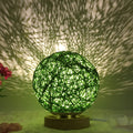 Hand-knit rattan ball table lamp with remote control on a wooden table, powered by USB cable.