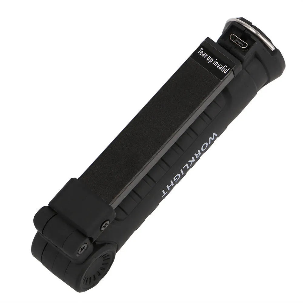 COB LED tactical flashlight in carbon-black finish with folding stand, magnet, and hanging hook on a metal surface
