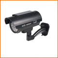 Black plastic solar-powered fake gun security camera with visible solar panel and spot light.