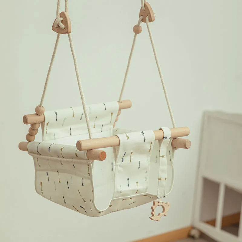 Cotton canvas baby swing chair with wooden seat and tassel decoration, hanging indoors.