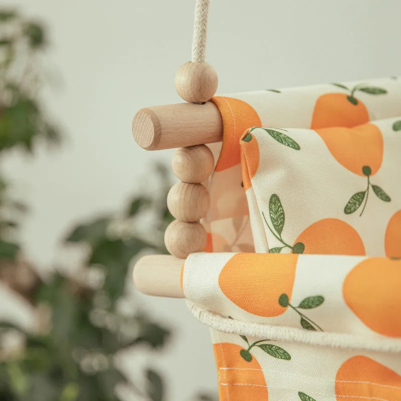 Cotton canvas baby swing chair with wooden seat and tassel decoration, hanging indoors.