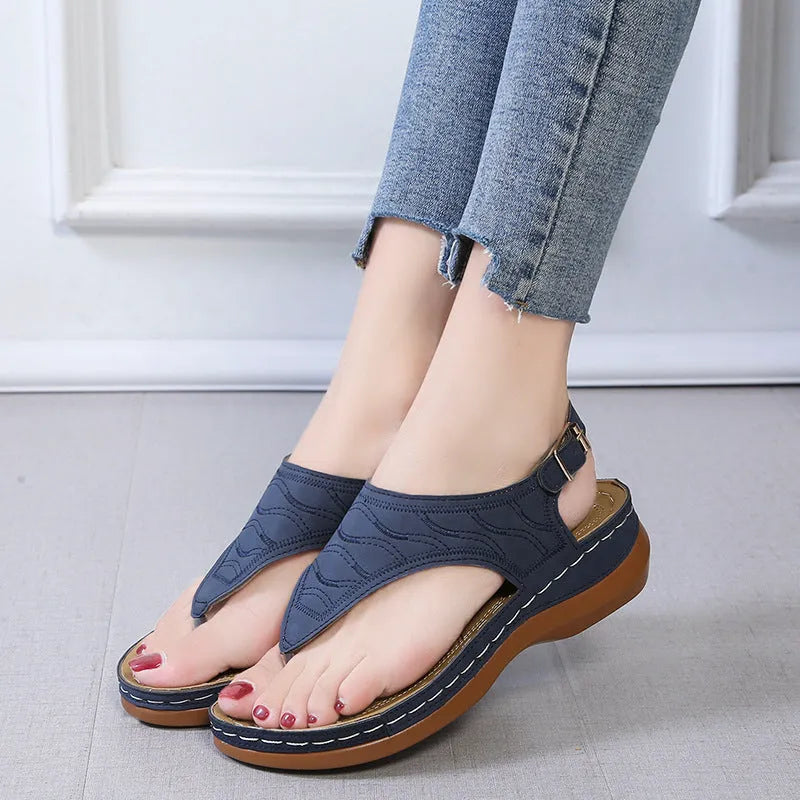 Women's beige wedge heel flip flop sandals with an adjustable buckle strap on a wooden deck.