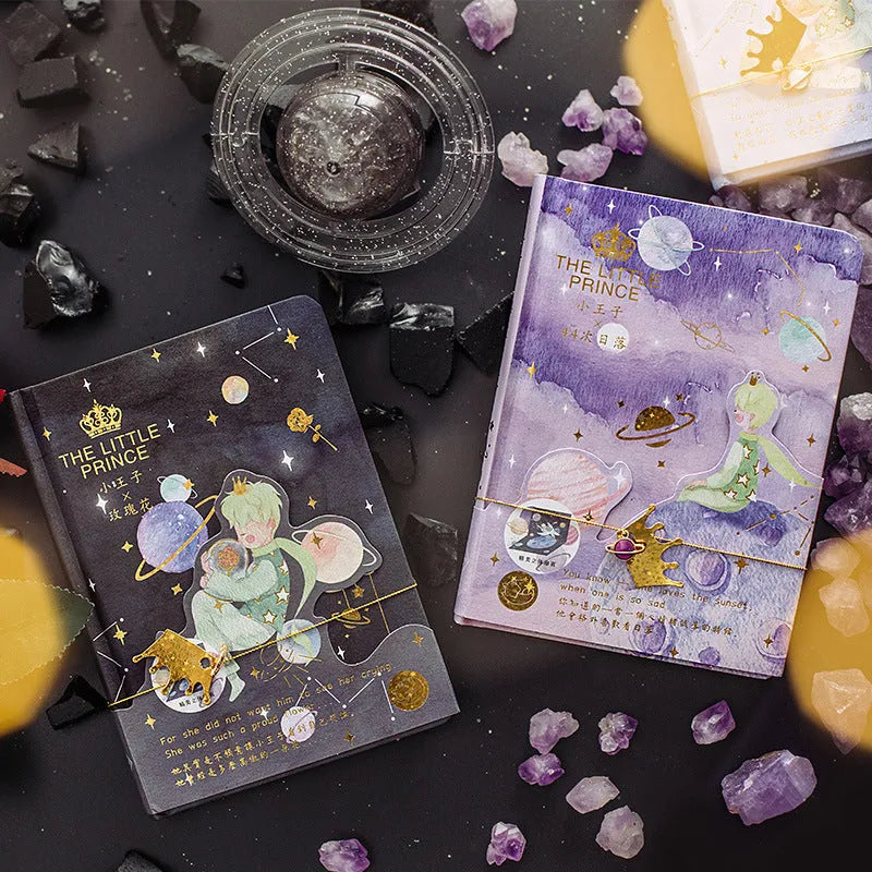 Hardback Little Prince notebook open on a table, showing one of four cover designs: sunset, bird, roses, or fox.