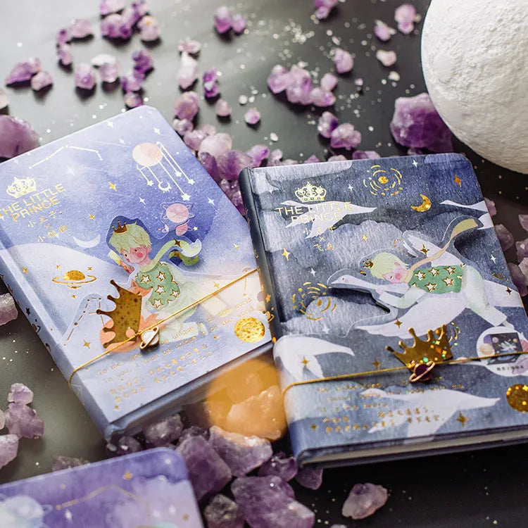 Hardback Little Prince notebook open on a table, showing one of four cover designs: sunset, bird, roses, or fox.