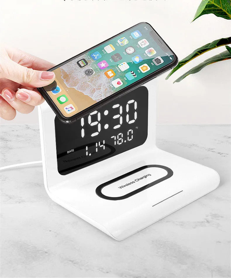White wireless charger alarm clock showing digital time, date, temperature and humidity display on a desk.