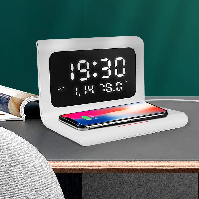 White wireless charger alarm clock showing digital time, date, temperature and humidity display on a desk.