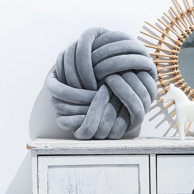 Square Nordic decorative cushion with a knotted ball design in caramel colour on a grey sofa.
