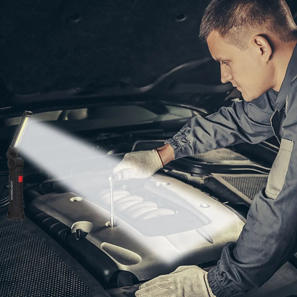 COB LED tactical flashlight in carbon-black finish with folding stand, magnet, and hanging hook on a metal surface