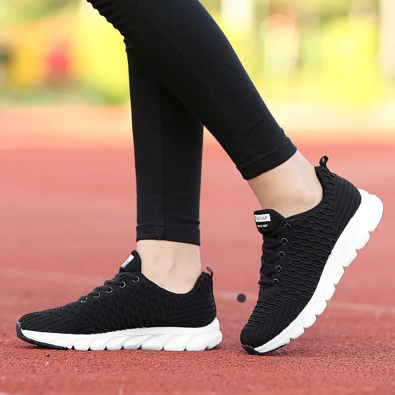 Women's running shoes in black, pink, and white with a fly weaving upper and wear-resistant outsole.