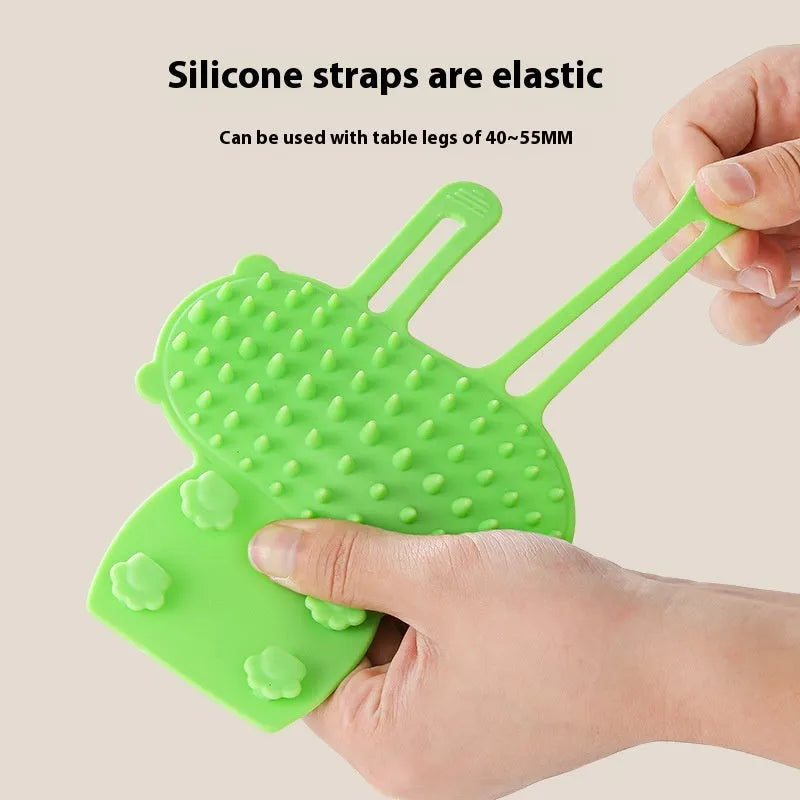 Silicone cat grooming comb with adjustable strap mounted on a table leg.
