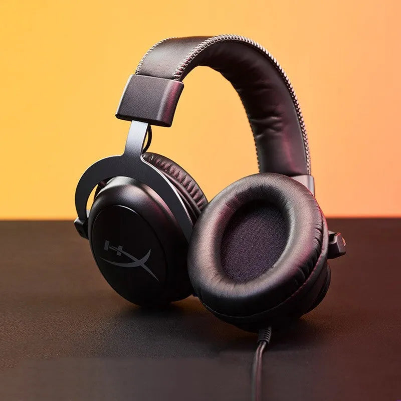 Black and red wired over-ear gaming headset with detachable microphone on a desk next to a USB sound card remote control.