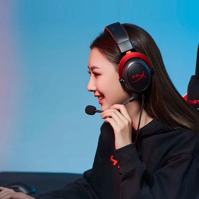 Black and red wired over-ear gaming headset with detachable microphone on a desk next to a USB sound card remote control.
