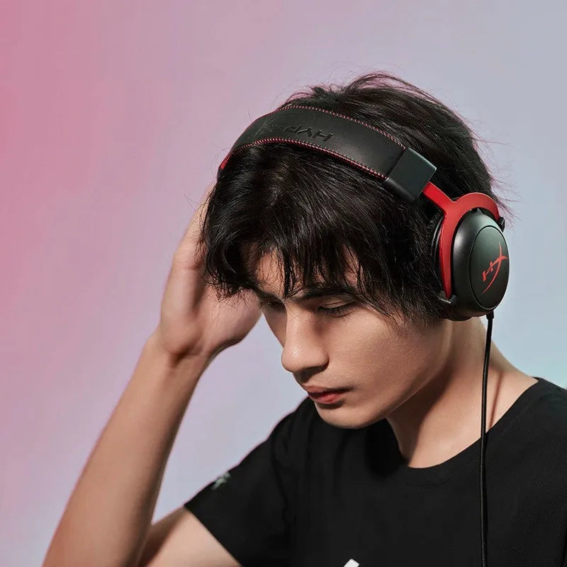 Black and red wired over-ear gaming headset with detachable microphone on a desk next to a USB sound card remote control.